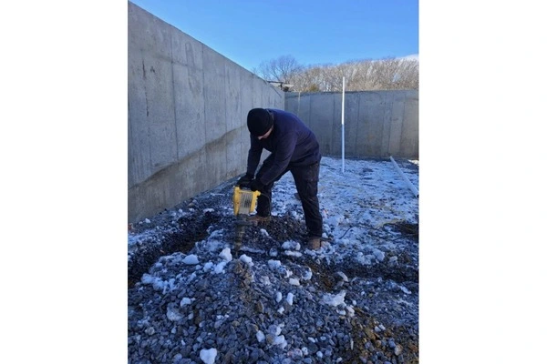 Plumber working outdoors in freezing winter conditions next to a concrete foundation wall
